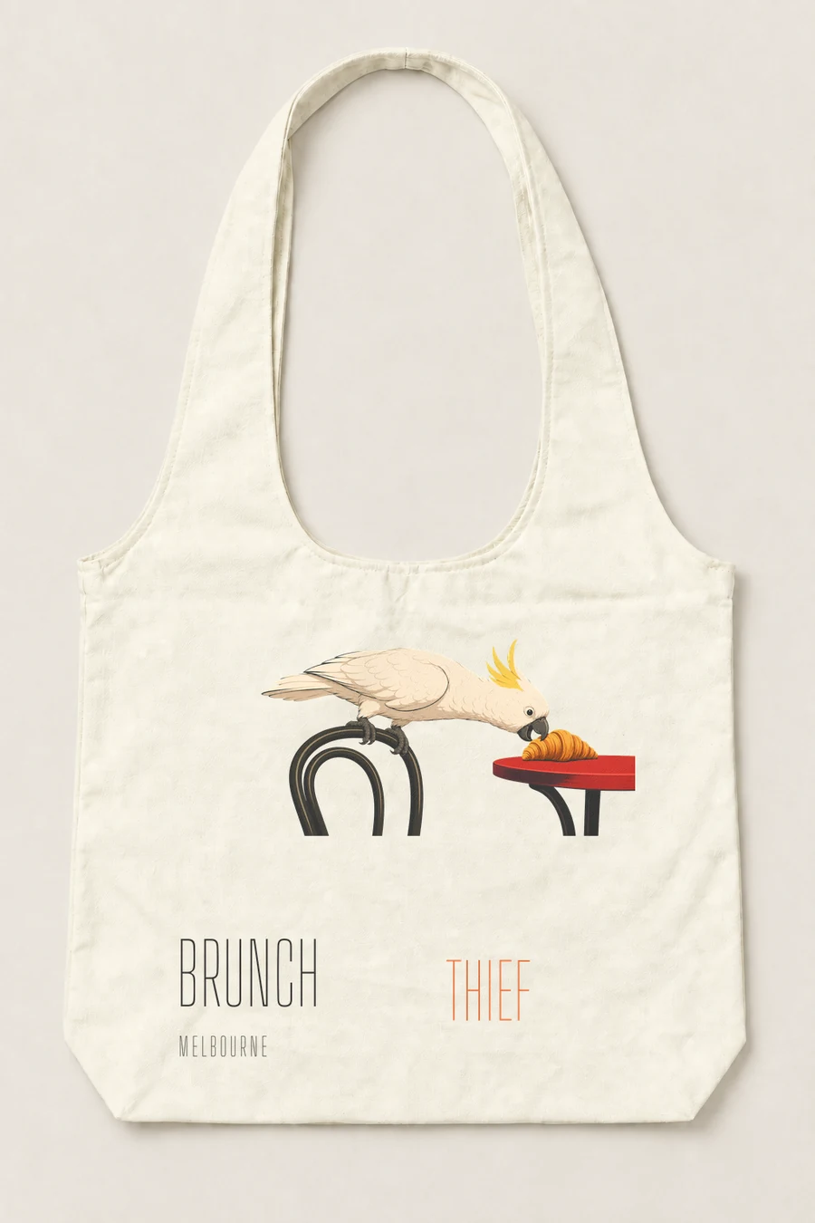 Brunch Thief artwork showing a cockatoo taking a croissant, rendered on the natural canvas tote